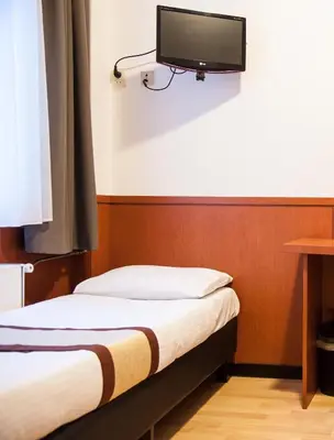 a room with two beds and a tv on the wall at Hotel Continental Amsterdam in Amsterdam