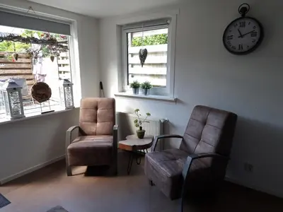 a living room with two chairs and a clock on the wall at De Blokhut in Egmond aan den Hoef