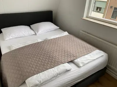 a bed with white sheets and pillows next to a window at Katwijk Center, 1 min away from the beach! in Katwijk aan Zee