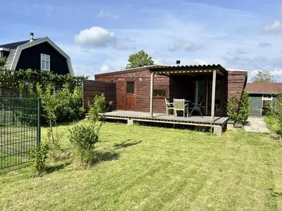 a small cabin with a deck in a yard at Vrijstaand chalet met veel buitenruimte en veranda in Zuid-Scharwoude