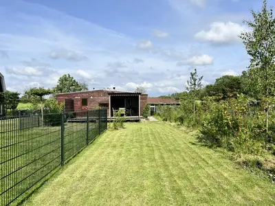 a fence in front of a house with a yard at Vrijstaand chalet met veel buitenruimte en veranda in Zuid-Scharwoude