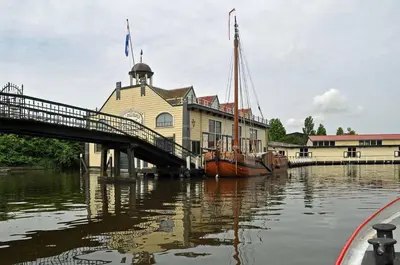a building with a bridge and a boat in the water at Vrijstaand chalet met veel buitenruimte en veranda in Zuid-Scharwoude