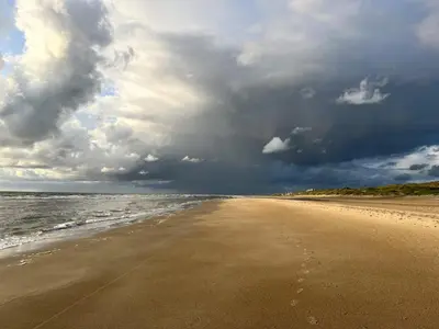 a sandy beach with a cloudy sky and the ocean at Vrijstaand chalet met veel buitenruimte en veranda in Zuid-Scharwoude