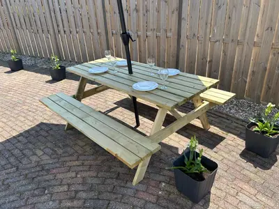 a wooden picnic table with an umbrella and a bench at Amsterdam Beach Apartment 17, incl Parking + Garden in Zandvoort