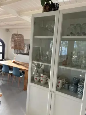 a white cabinet with dishes in it next to a table at Have a nice stay! - Vakantiehuis BijSaar in Noordwijk