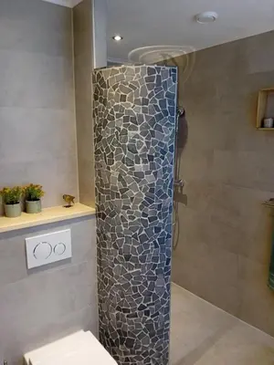 a shower in a bathroom with a stone wall at Oudaen 36 in Lelystad