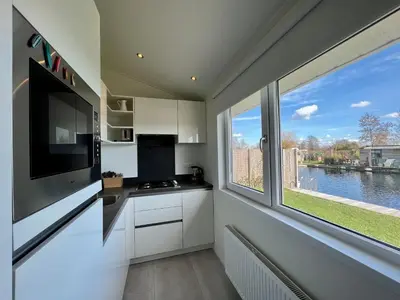 a kitchen with white cabinets and a large window at NEW - The Surf Shack - on a lake near Amsterdam! in Vinkeveen