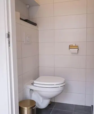 a bathroom with a white toilet and a trash can at Strand83 in Egmond aan Zee