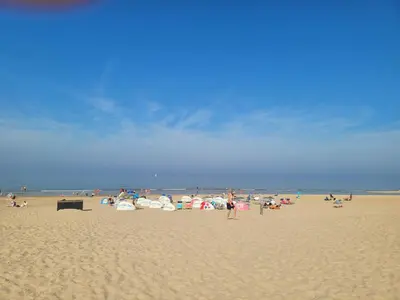 a group of people standing on a beach at Appartement Canberra. in Bergen aan Zee