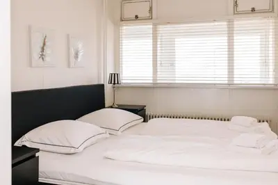 a white bed with white pillows and a window at Appartement Babette in Zandvoort