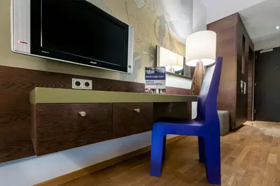 a desk with a tv and a blue chair at Hotel Artemis Amsterdam in Amsterdam