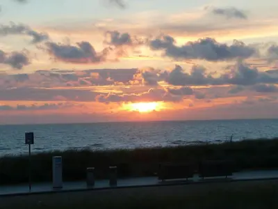 a sunset over the ocean with two benches on a road at Sterflat 39 in Egmond aan Zee
