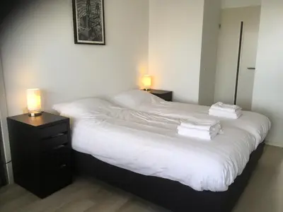 a bedroom with a bed with white sheets and two lamps at Sterflat 45 in Egmond aan Zee