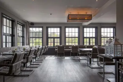 a dining room with tables and chairs and windows at Fletcher Boutique Hotel Duinoord in Wassenaar
