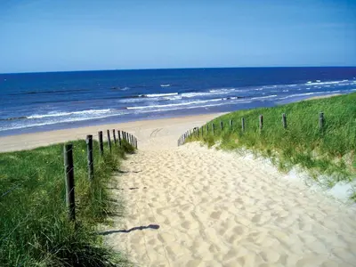 a sandy beach next to the ocean with a fence at Fletcher Boutique Hotel Duinoord in Wassenaar