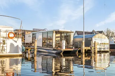 a boat is docked at a dock in the water at Charming Tiny Houseboat Escape Near Amsterdam by Weltevreden Experience in Kortenhoef