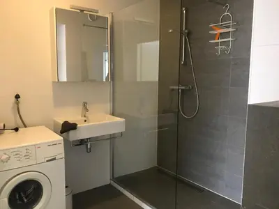 a bathroom with a shower and a sink and a washing machine at Sterflat 59 in Egmond aan Zee