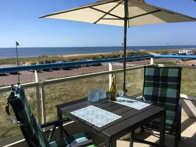 a table and chairs with an umbrella and the beach at Sterflat 65 in Egmond aan Zee