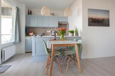 a kitchen with blue cabinets and a table and chairs at Sterflat 63 in Egmond aan Zee