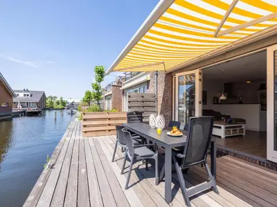a wooden deck with a table and chairs next to the water at Assum Great in Uitgeest