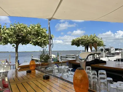a table with glasses on it next to the water at Holiday Home De Meerparel by Interhome in Uitgeest