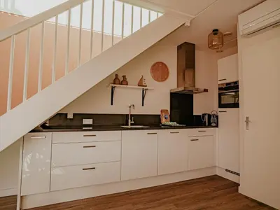 a kitchen with white cabinets and a staircase at Holiday Home De Meerparel by Interhome in Uitgeest