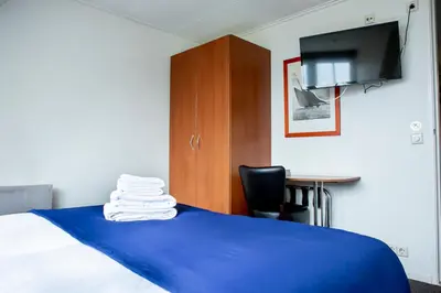 a bedroom with a bed with a blue blanket and a desk at Hotel Café Restaurant Heineke in Loosdrecht