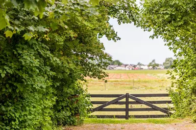 a wooden gate in a field with a fence at Het Kamphuis, landelijk slapen in Heerhugowaard