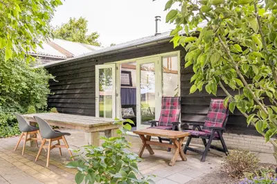 a patio with chairs and a wooden table and a table and chairs at Het Kamphuis, landelijk slapen in Heerhugowaard