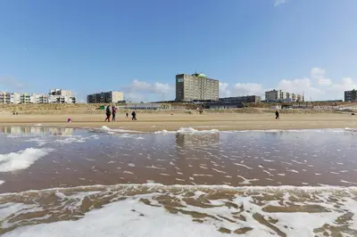 a sandy beach with people walking on the beach at Beachhotel Zandvoort by Center Parcs in Zandvoort