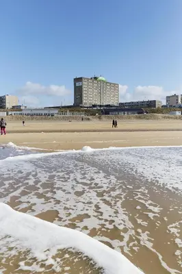 a beach with snow on the sand and people walking on the beach at Beachhotel Zandvoort by Center Parcs in Zandvoort
