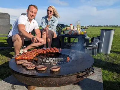 a man and a woman cooking food on a grill at Camping de Speld in Nieuwkoop