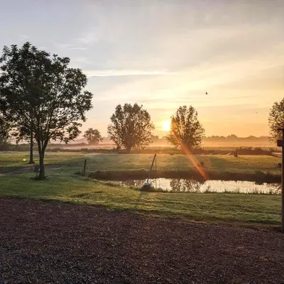 a sunset over a field with a pond at Camping de Speld in Nieuwkoop