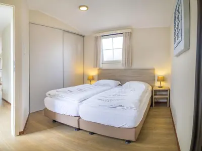 two beds in a small bedroom with a window at Chalet in Noordwijk near the Beach in Noordwijk aan Zee