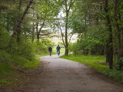 two people riding bikes down a dirt road at Chalet in Noordwijk near the Beach in Noordwijk aan Zee
