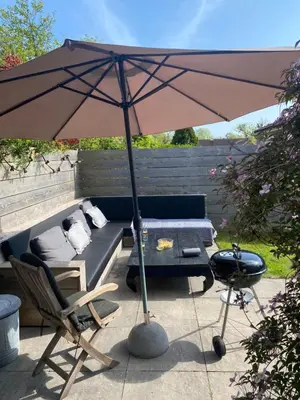 an umbrella on a patio with a couch and a chair at Huis Egmond in Egmond aan den Hoef