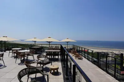 a patio with tables and chairs and the beach at Strandhotel Het Hoge Duin in Wijk aan Zee