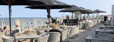 a group of people sitting at tables with umbrellas on the beach at De Schelp 58 in Zandvoort