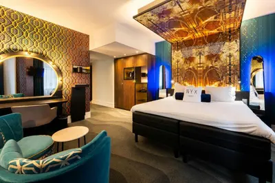 a hotel room with a bed and chairs and a mirror at NYX Hotel Amsterdam Rembrandt Square in Amsterdam