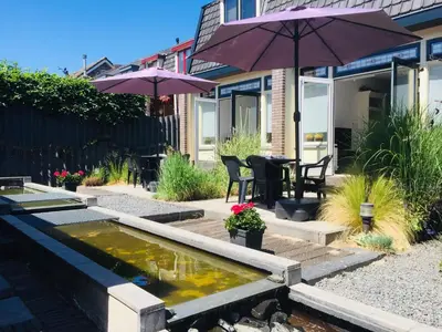 a backyard with a pond with an umbrella and chairs at Holiday in Spakenburg Groof in Spakenburg