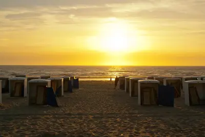 a row of beach chairs on the beach at sunset at Het Eerste Huisje vacation home in Noordwijk aan Zee
