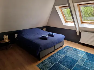 a bedroom with a bed with blue sheets and two windows at Aan de Burgwal in Enkhuizen