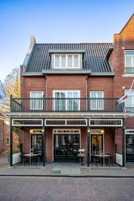 a red brick building with a balcony and tables at Hotel Aalsmeer in Aalsmeer