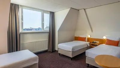 a hotel room with two beds and a window at Hotel Aalsmeer in Aalsmeer