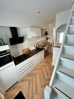 a kitchen with white cabinets and a wooden floor at Tiny House in center Aalsmeer I Close to Schiphol & Amsterdam in Aalsmeer
