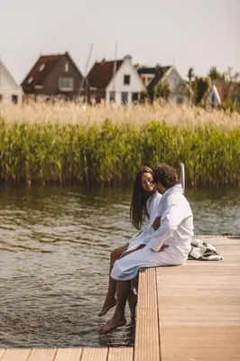 a man and woman sitting on a dock by the water at De Durgerdam, Amsterdam in Amsterdam