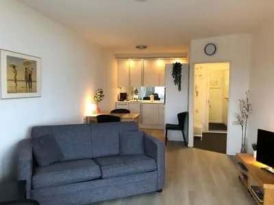 a living room with a blue couch and a kitchen at Sterflat 67 in Egmond aan Zee