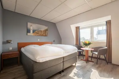 a bedroom with a bed and a table and a window at Two Brothers Hotel Astoria in Noordwijk aan Zee