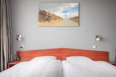 a bedroom with two white beds and a painting on the wall at Two Brothers Hotel Astoria in Noordwijk aan Zee