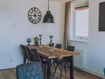 a dining room table with chairs and a clock on the wall at Westergeest in Uitgeest